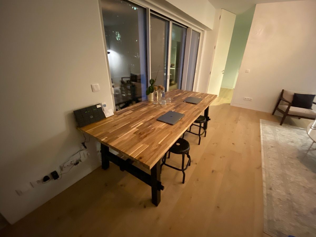 Two Macs on a large wooden desk with stools underneath. A place with cork bottles placed in the middle.