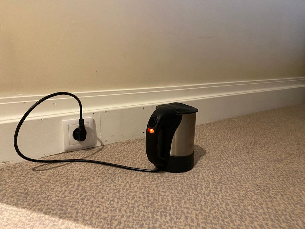 A travel kettle placed on a carpet plugged into a socket near the floor