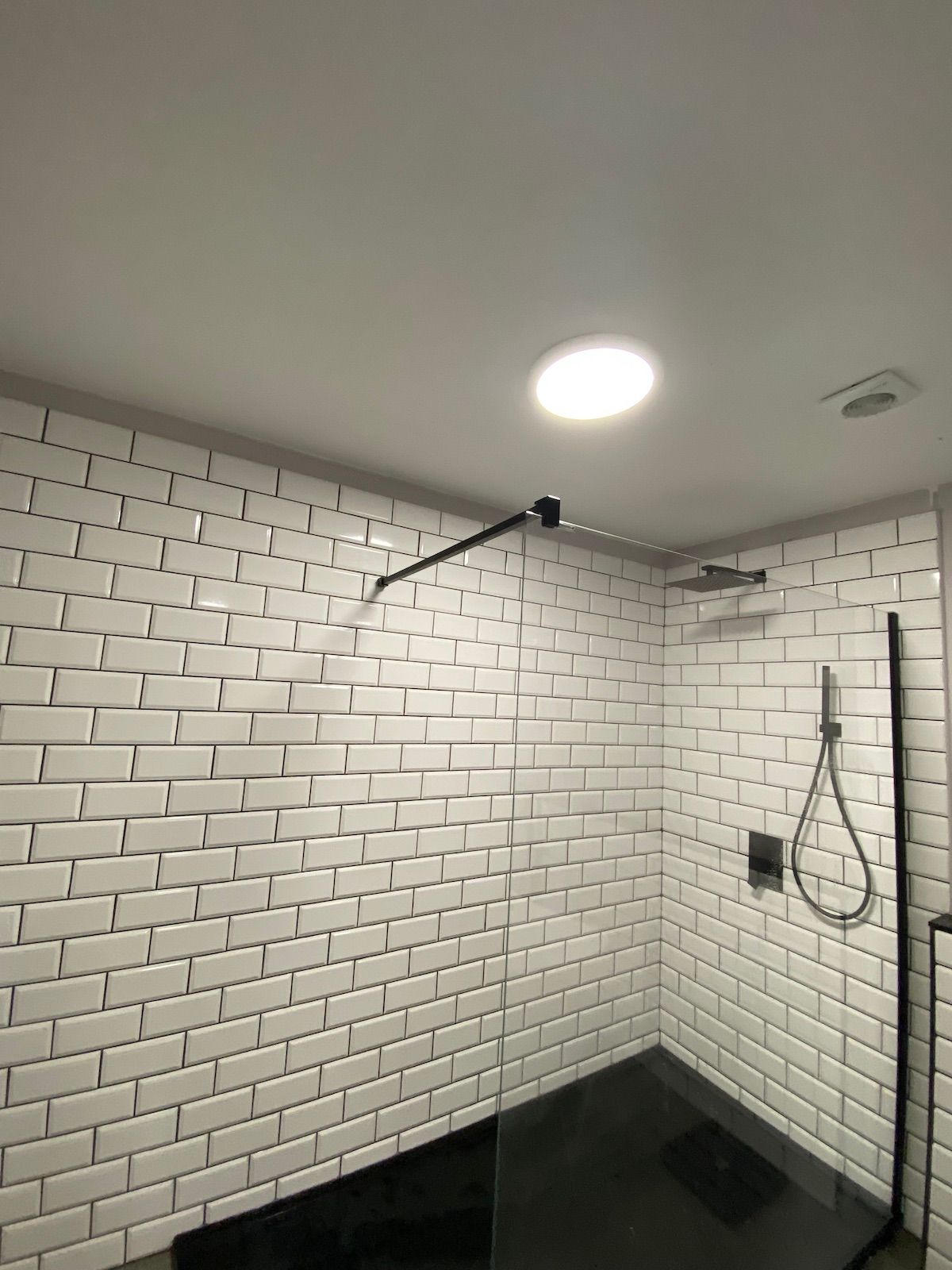 A shower with a glass divider and white subway tiles.